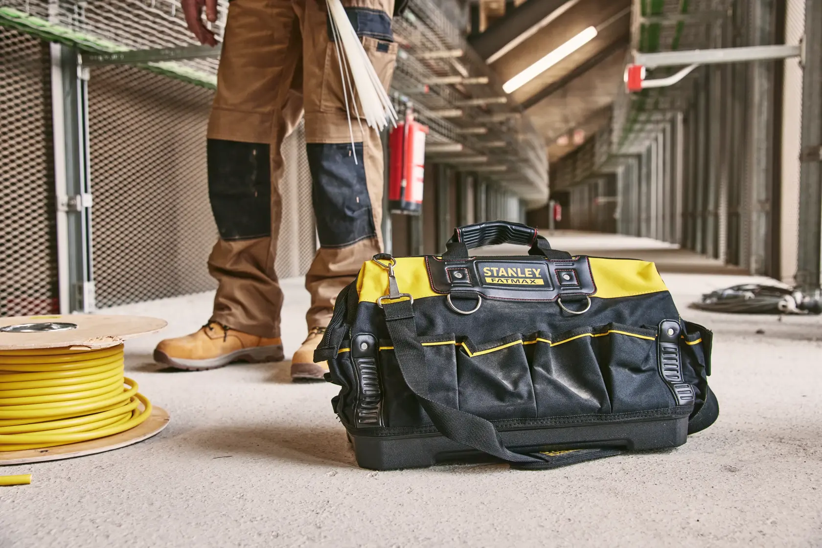 Sac à outils STANLEY 1-93-950 noir et jaune avec poignées, posé sur un chantier à côté d’une bobine de câble.
