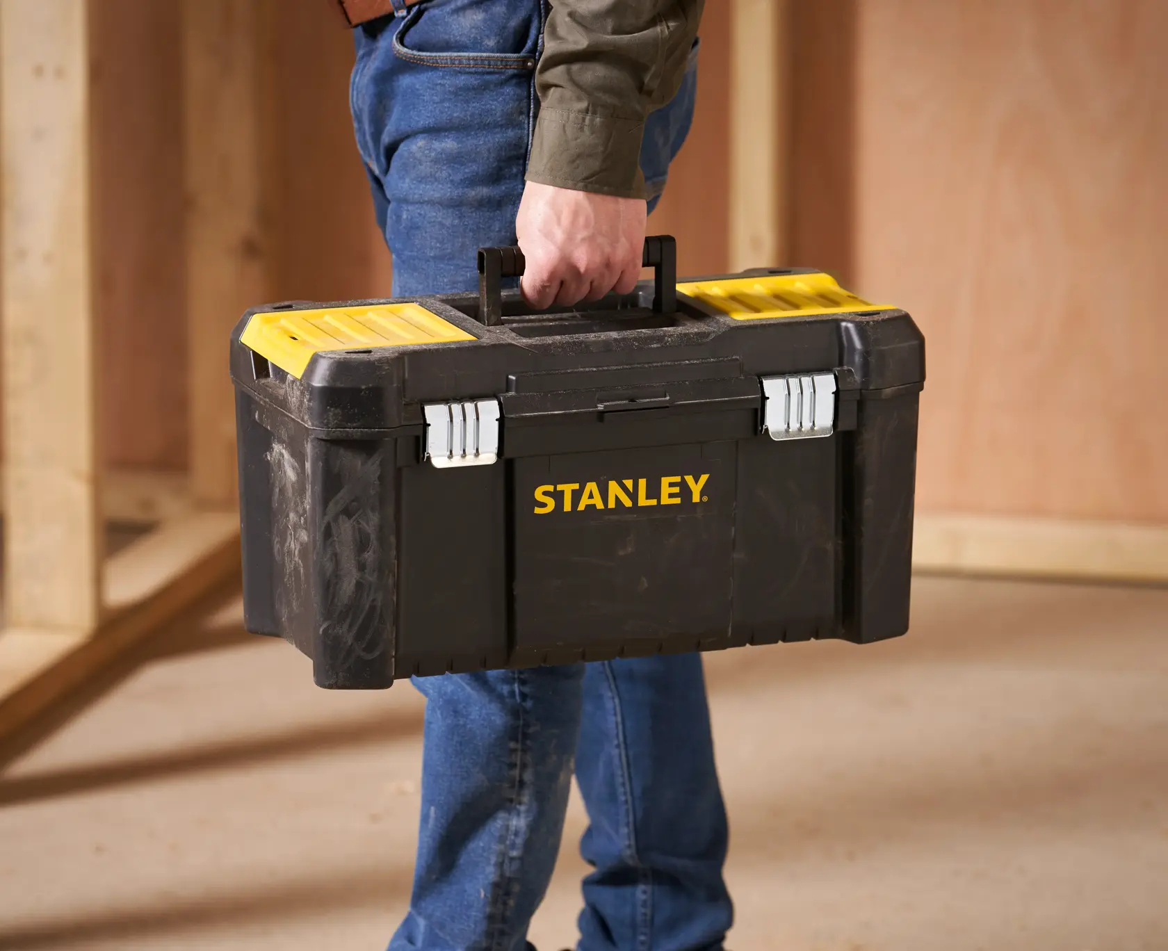 Boîte à outils Stanley STST1-75521 noire et jaune portée par une personne, dans un atelier.