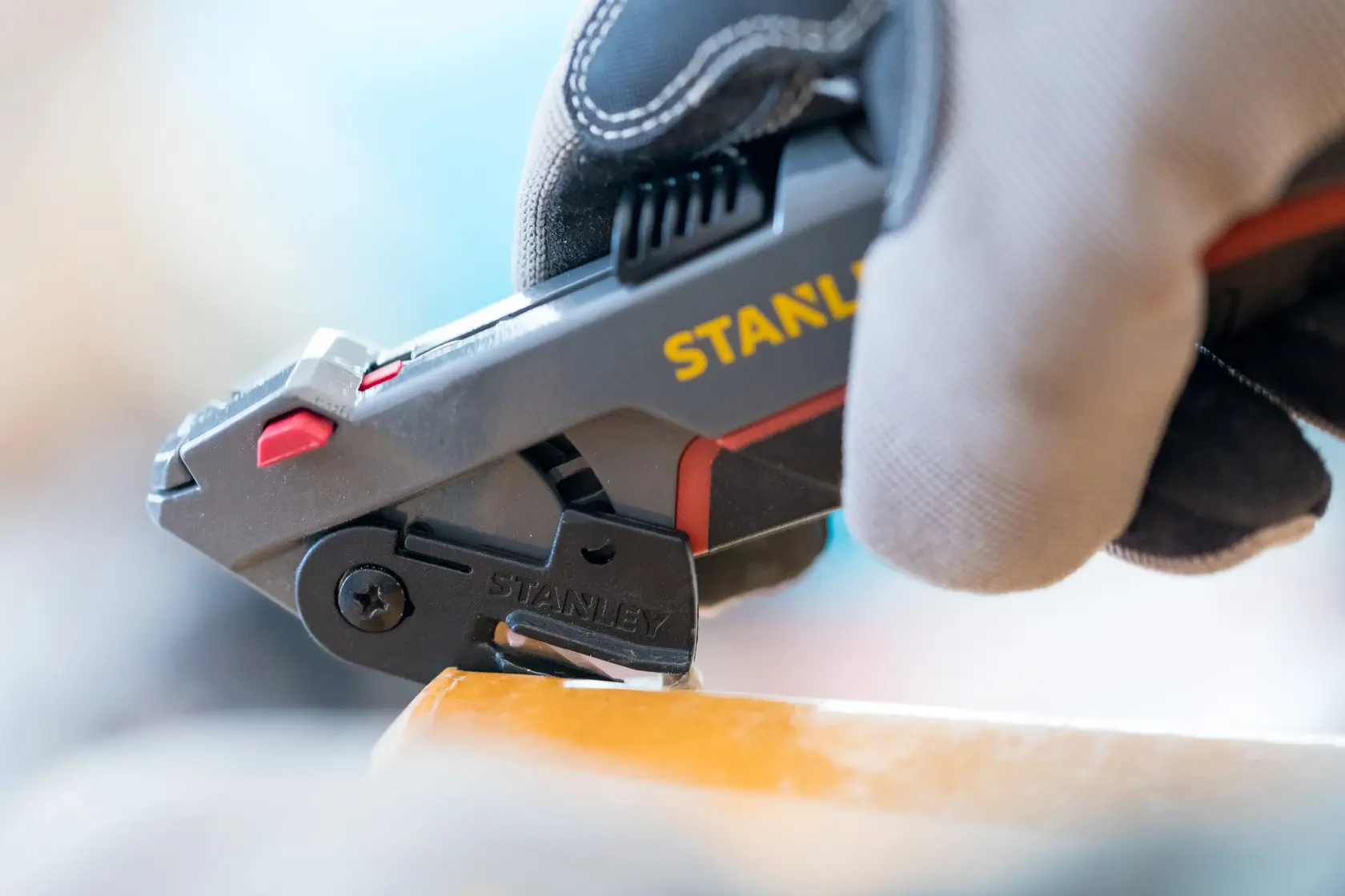 Cutter utilitaire STANLEY 0-10-242 en utilisation, vue rapprochée, main gantée tenant l’outil, coupant du matériau.