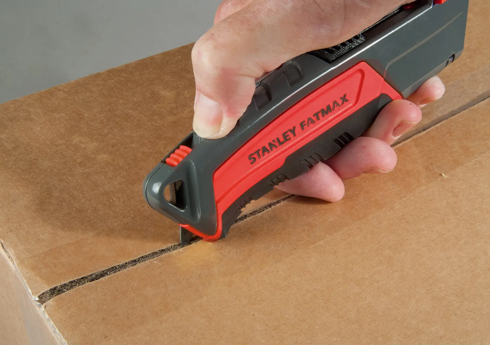 Cutter STANLEY 0-10-242 utilisé pour couper une boîte en carton, gros plan sur la main tenant l’outil rouge et noir.