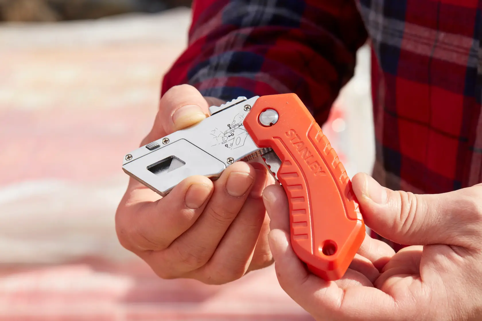 Stanley 0-10-243 couteau utilitaire pliant avec poignée orange présenté en main à l’extérieur.