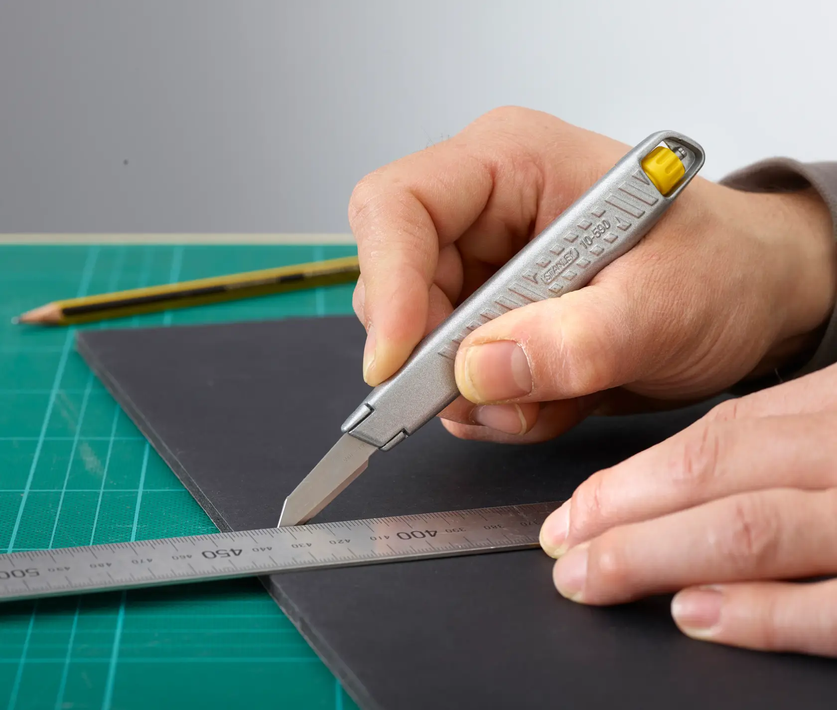 Photo of STANLEY 0-10-590 utility knife cutting black board with ruler on green mat.
