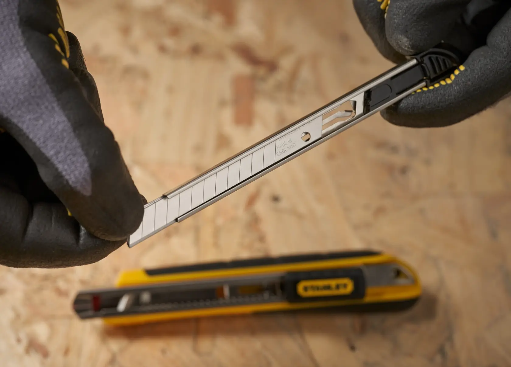 Foto der STANLEY 0-11-300 Abbrechklinge für Universalmesser im Austausch, mit Handschuhen, auf Holzoberfläche.
