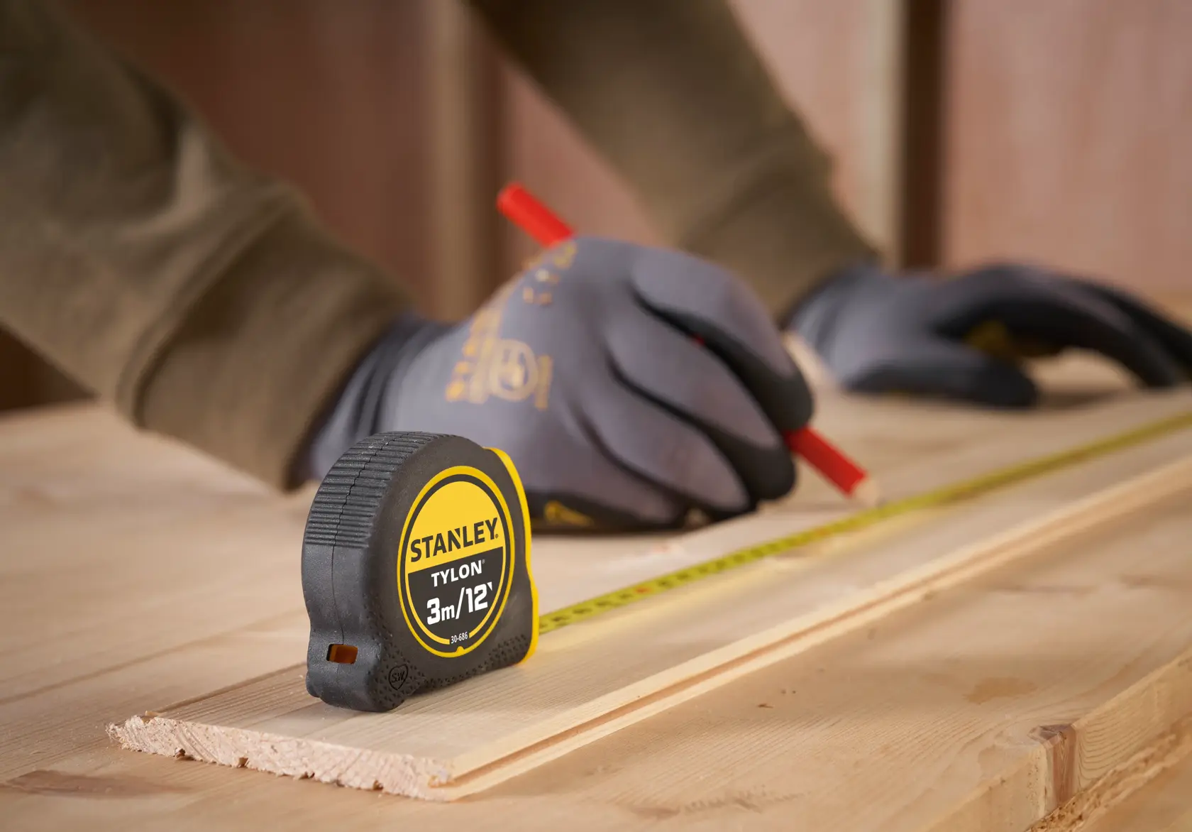 STANLEY 0-30-686 tape measure on wood with gloved hands marking measurements, product in use.
