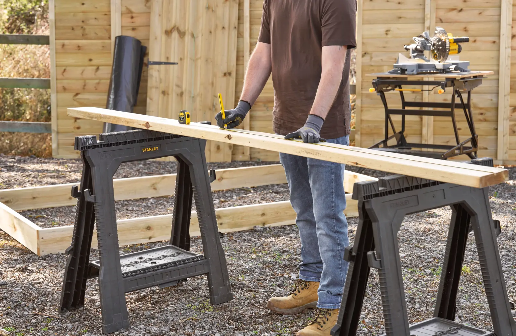STANLEY 0-30-687 folding saw horse pair supporting wood board in outdoor workspace, person measuring board.
