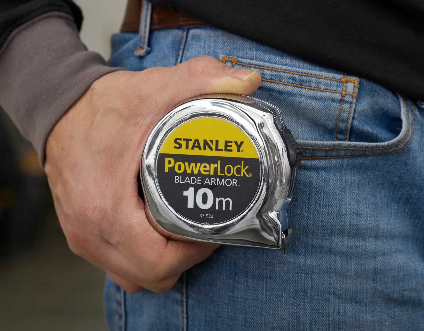 Photo du STANLEY PowerLock Blade Armor mètre ruban 10m SKU 0-33-532 tenu près d’un jean bleu.