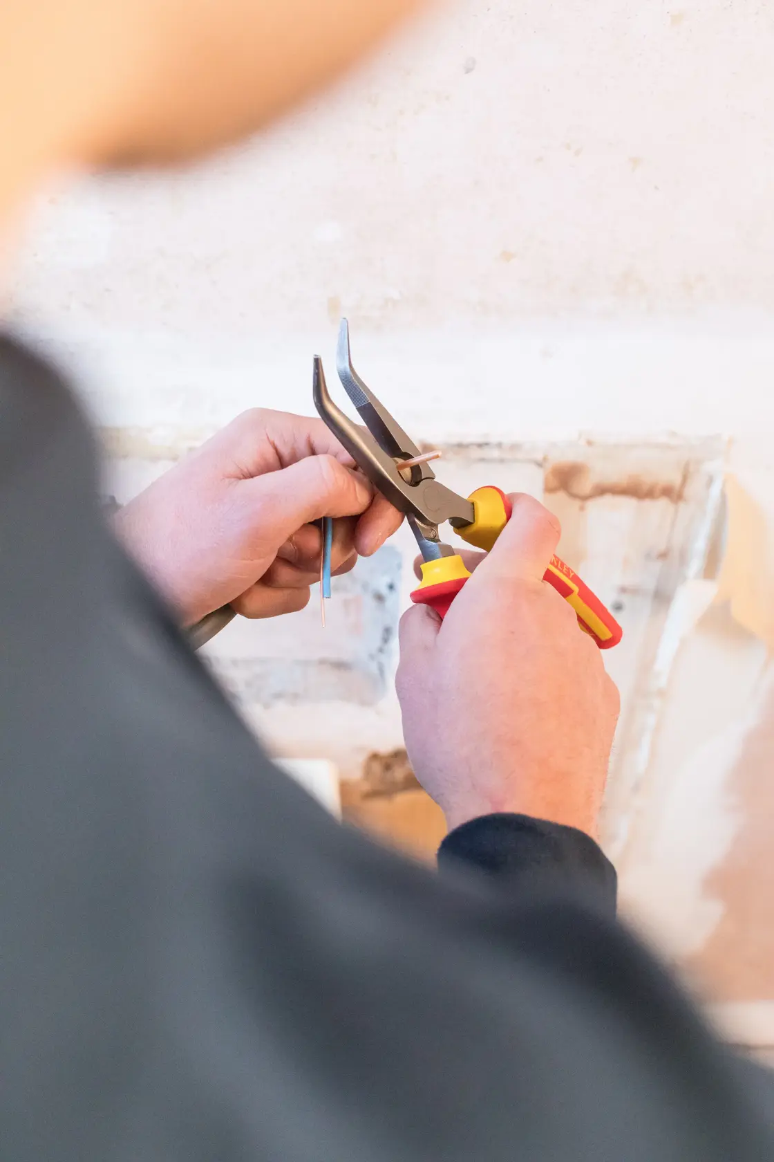 STANLEY 0-84-008 pliers with yellow and red handles, held by hand, close-up in work setting.