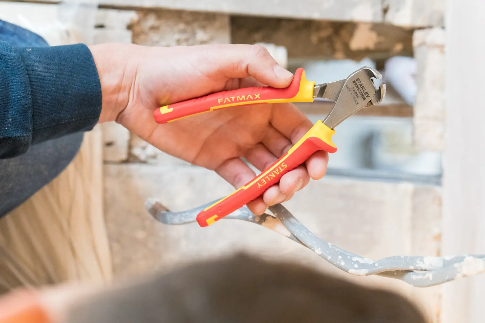 Photo of STANLEY 0-84-016 insulated pliers with red and yellow handles held by a hand, used on metal wire.