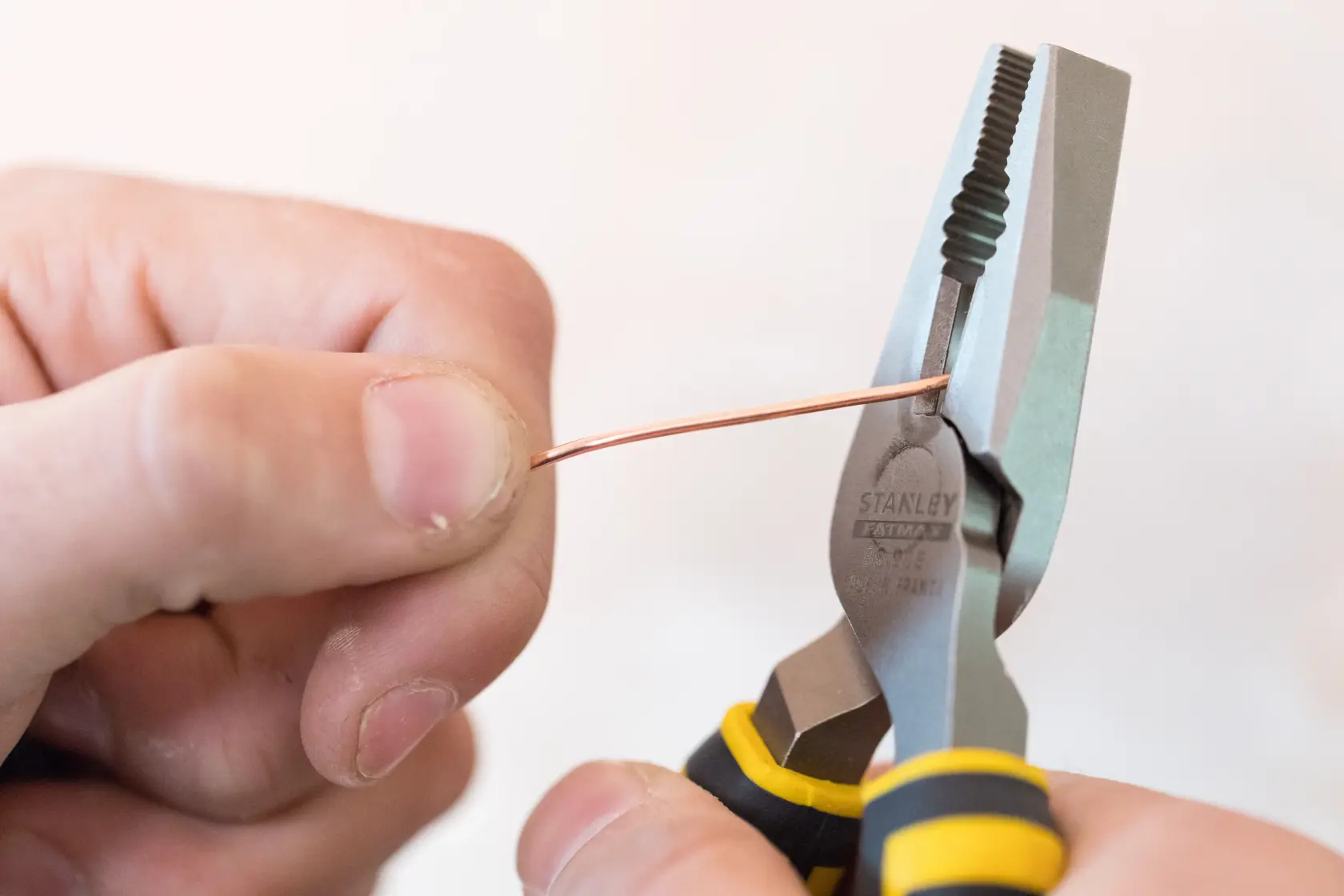 Stanley 0-89-866 pliers holding a copper wire, close-up view, black and yellow handle.