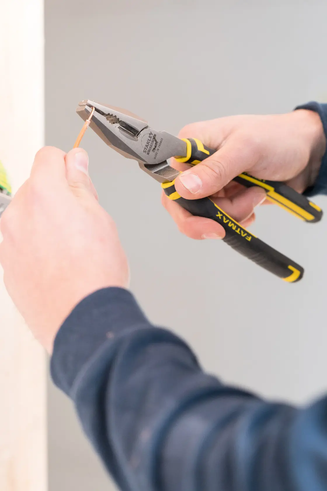 STANLEY 0-89-868 pliers being used to cut wire, close-up of black and yellow tool in hand.