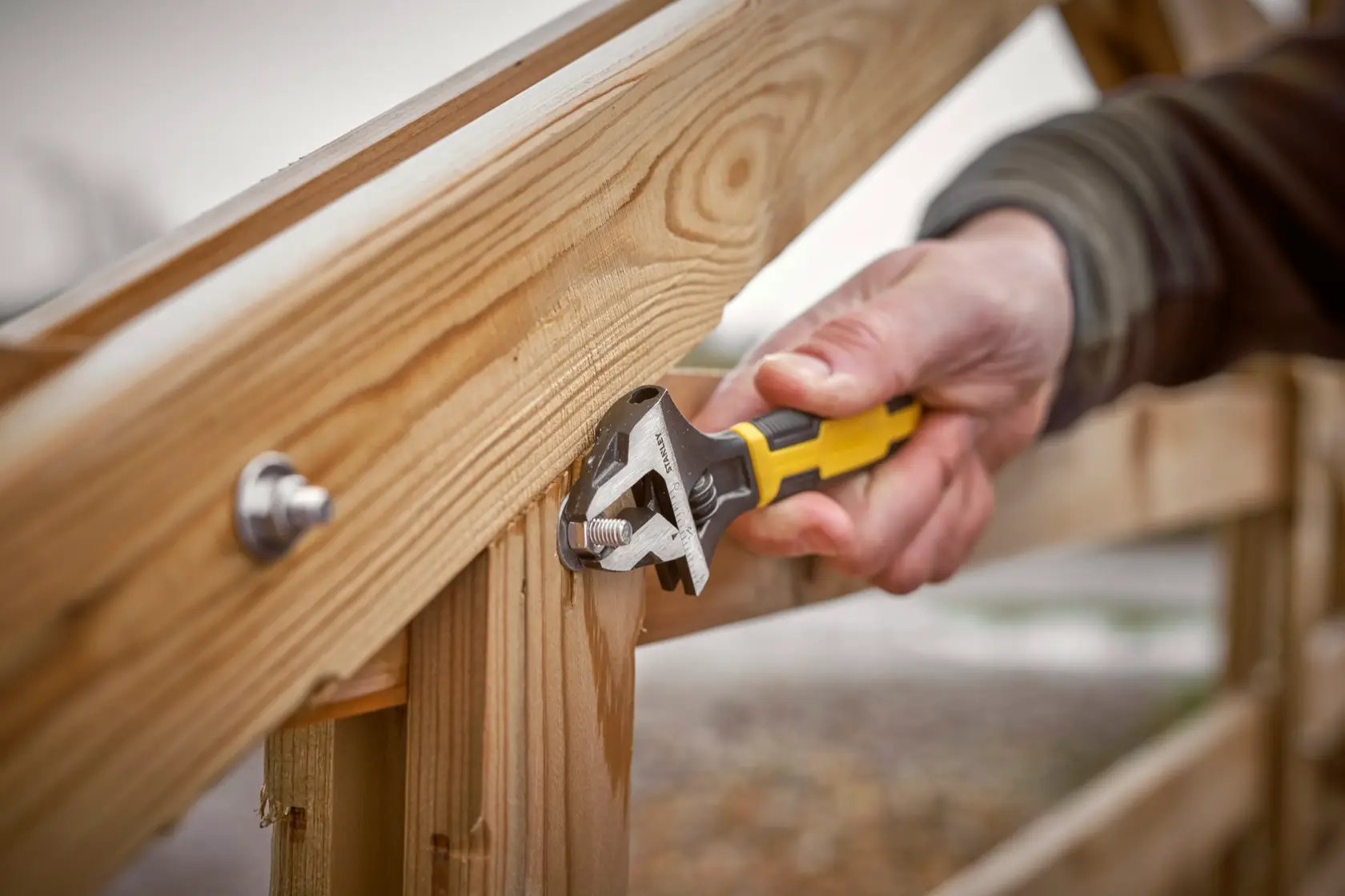 Photo of STANLEY 0-90-948 adjustable wrench tightening bolt on wooden fence outdoors.