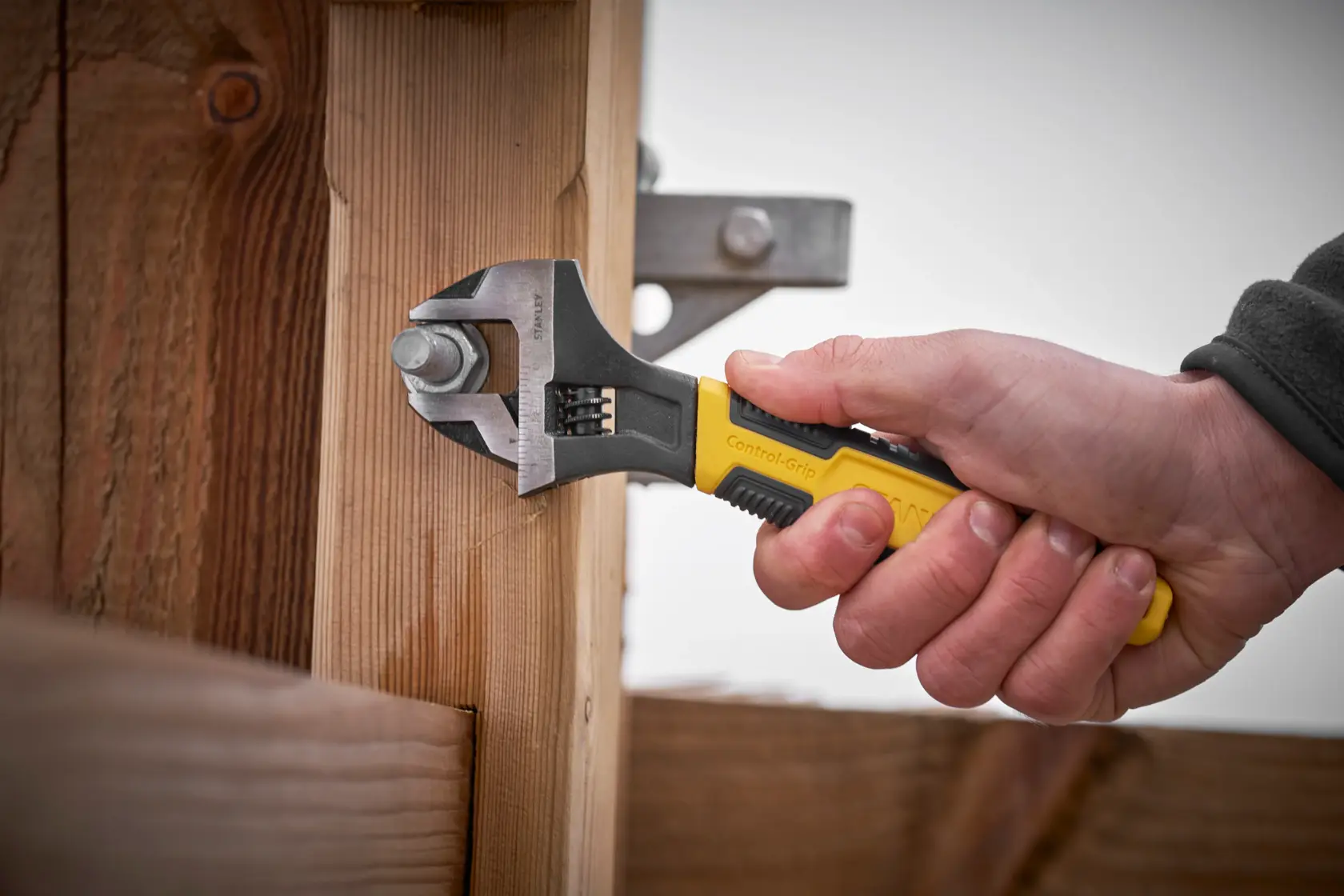 STANLEY 0-90-950 adjustable wrench with yellow grip tightening bolt on wooden beam, side angle.