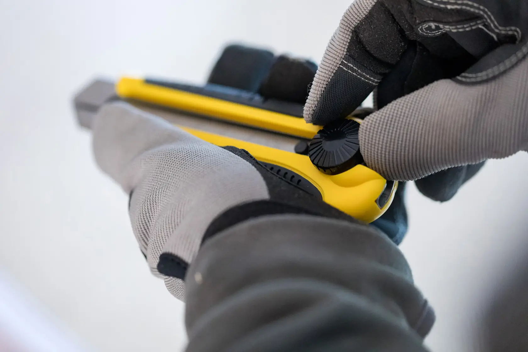 Cutter STANLEY 1-10-425 en utilisation, gros plan sur des mains gantées ajustant le cutter jaune.