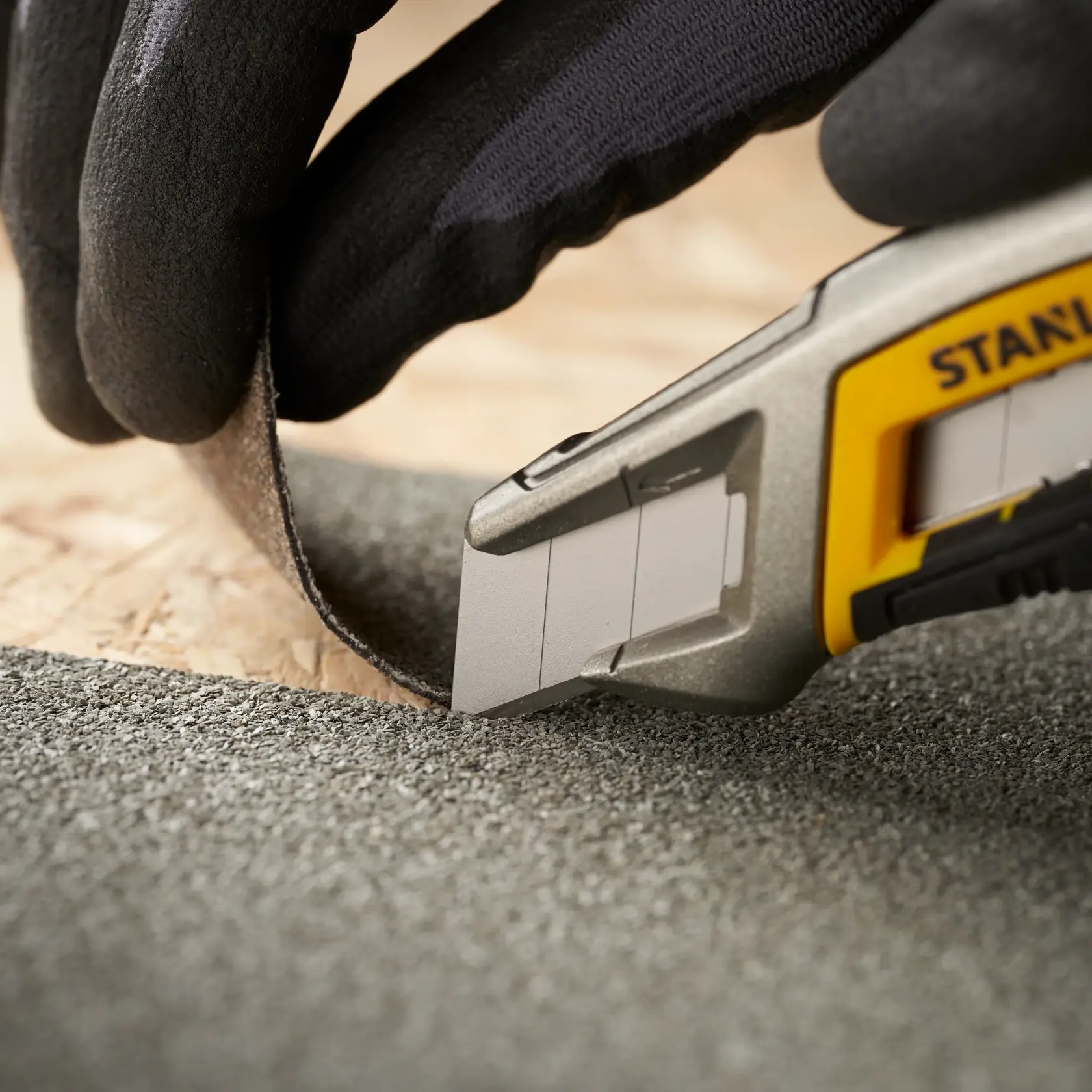 STANLEY 1-11-301 Universalmesser schneidet strukturiertes Material, Nahaufnahme mit Handschuh.