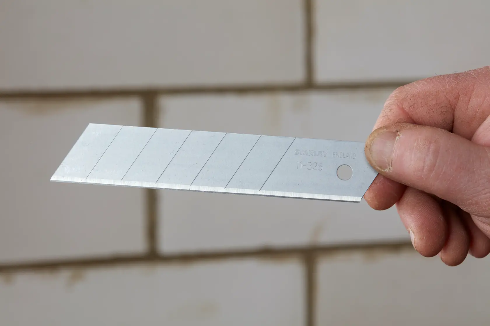 STANLEY 1-11-325 snap-off utility blade held in hand, silver finish, segmented design, photography.