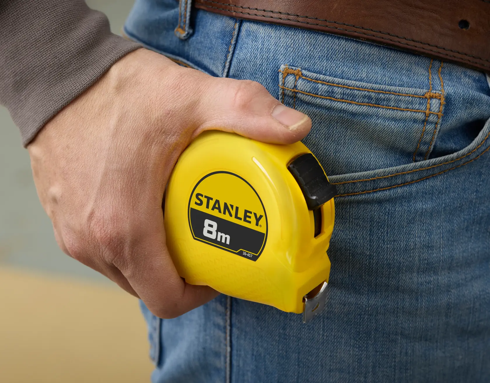 STANLEY 1-30-457 yellow 8m tape measure held by hand near jeans pocket, close-up.