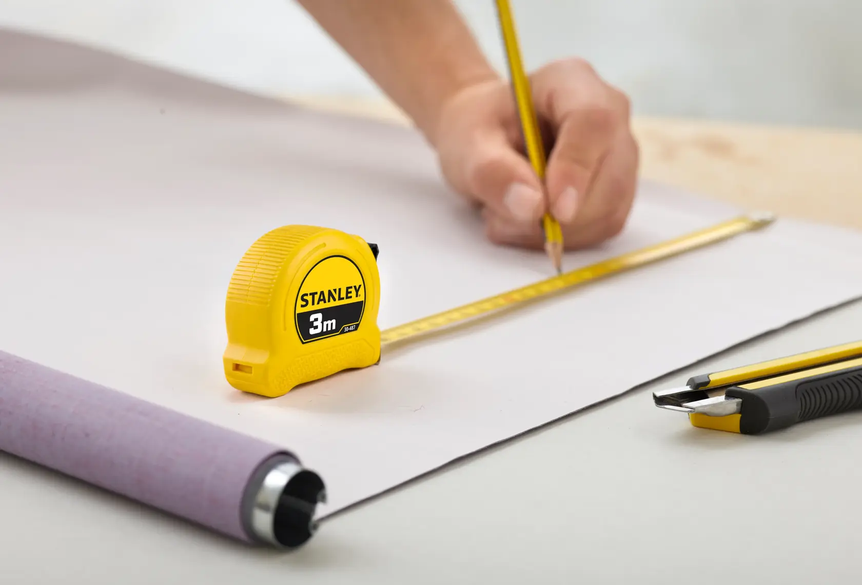 Photo of STANLEY 1-30-487 tape measure on table with pencil, cutter, and drawing in workspace.