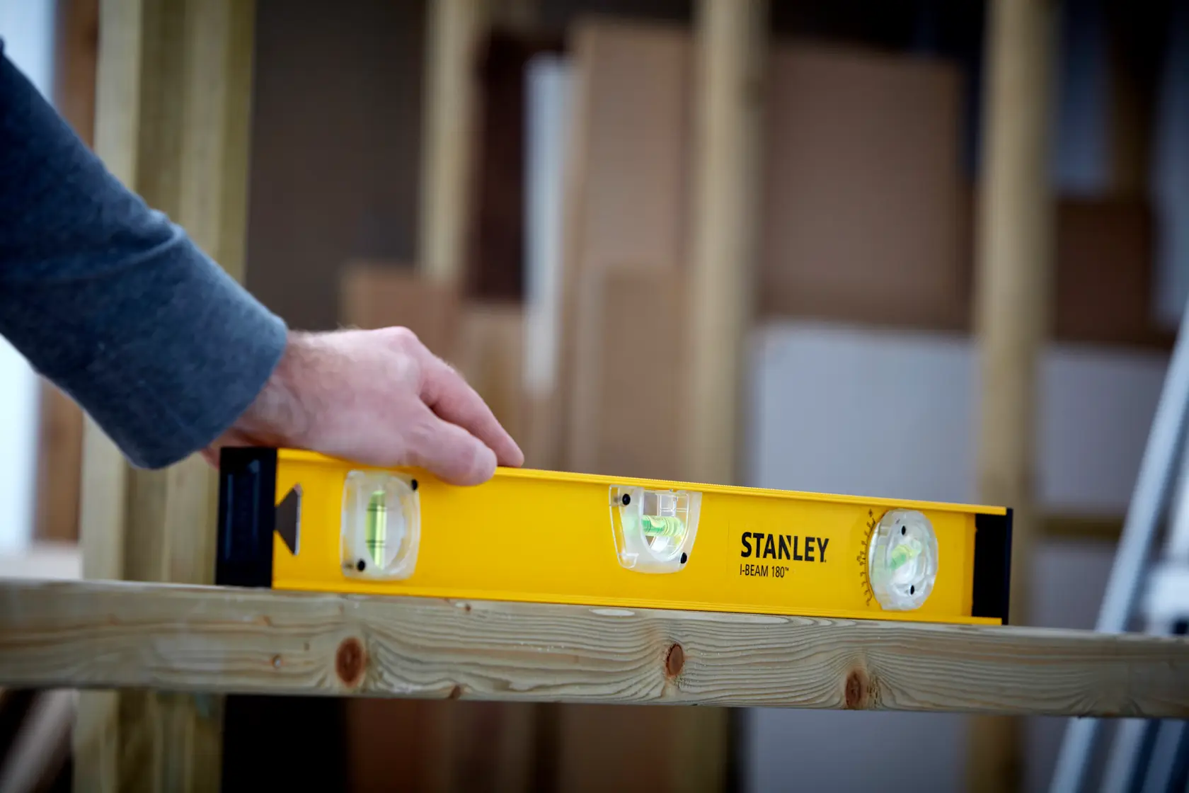 STANLEY 1-42-920 spirit level in use on wooden beam, yellow body with three vials, product in action.