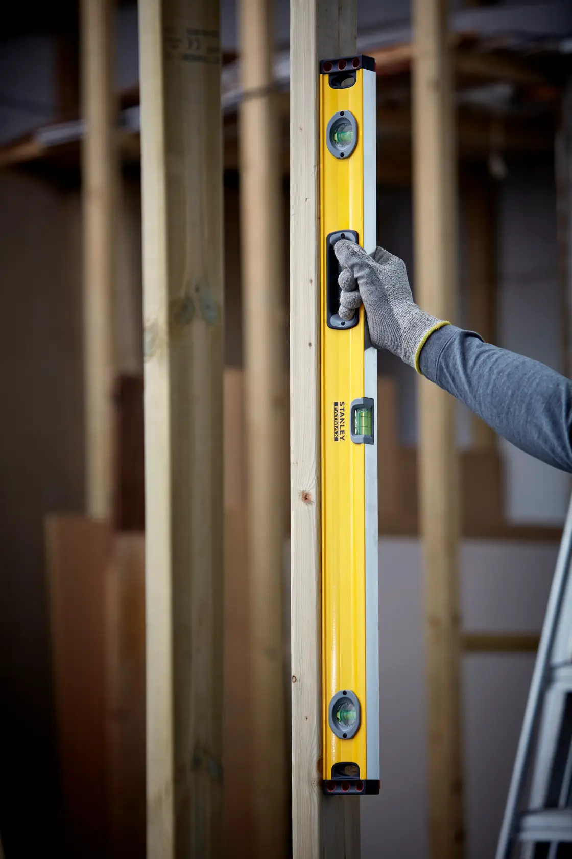 STANLEY 1-43-536 spirit level held vertically against wooden beam, gloved hand showing usage on construction site.