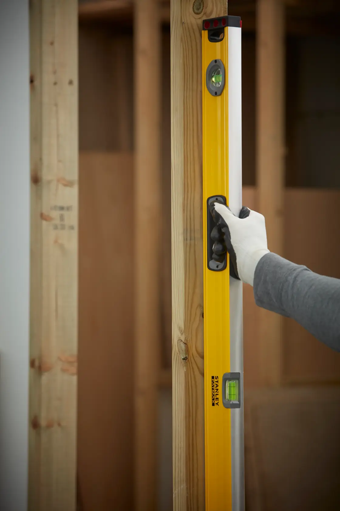 STANLEY 1-43-548 spirit level held by gloved hand against wooden beam, indoor construction setting.