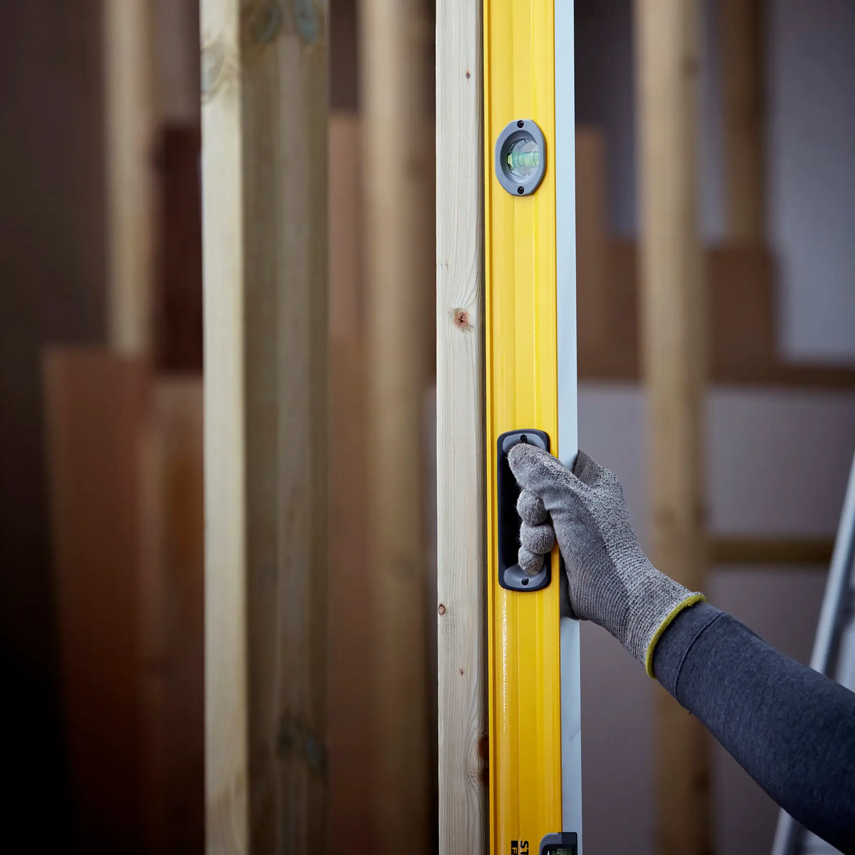 Niveau à bulle STANLEY 1-43-572 en utilisation, corps jaune avec main gantée tenant la poignée, fond de chantier.