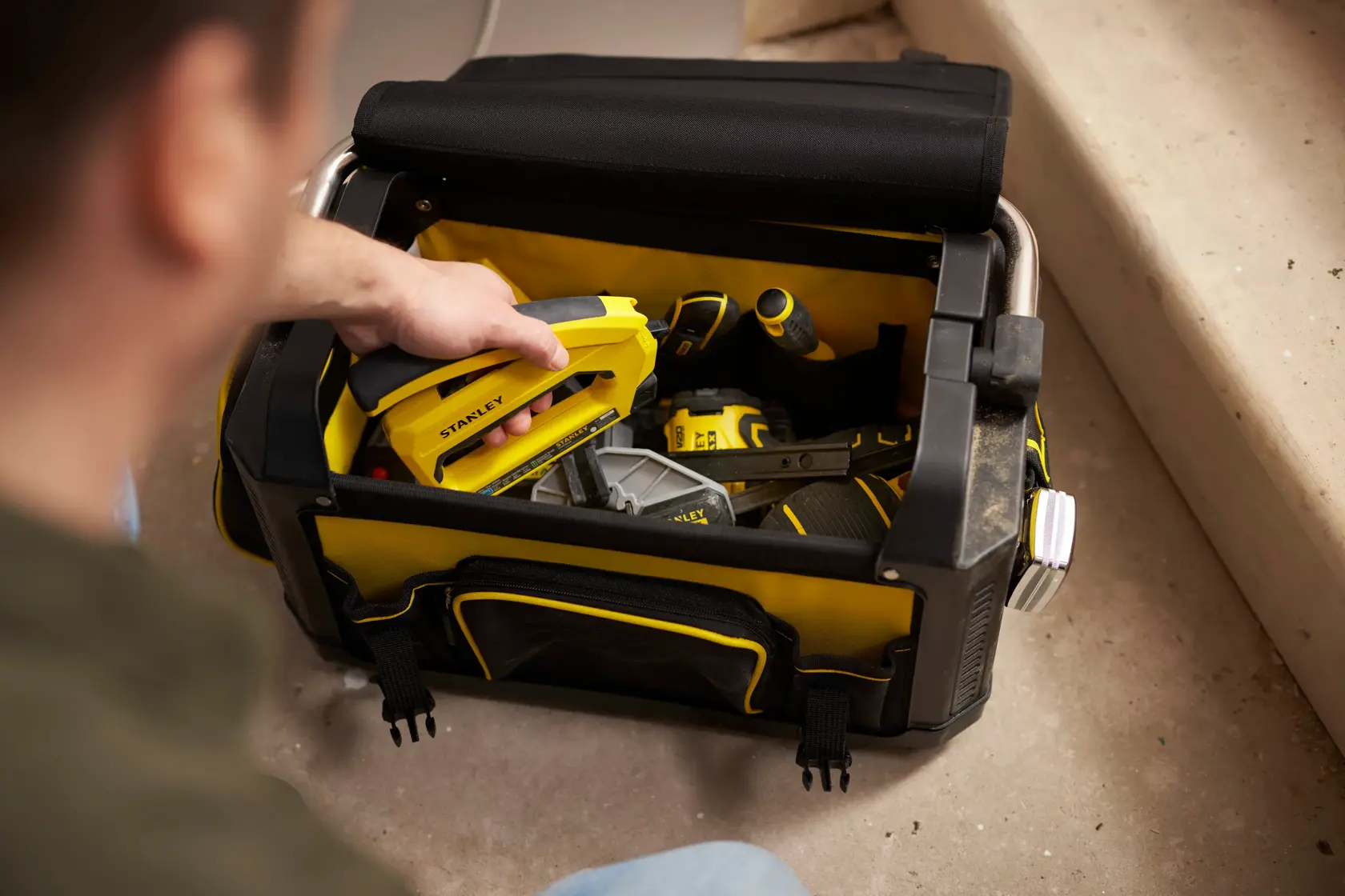 Photo of STANLEY 1-79-213 tool bag with open top, containing yellow and black hand tools on the floor.