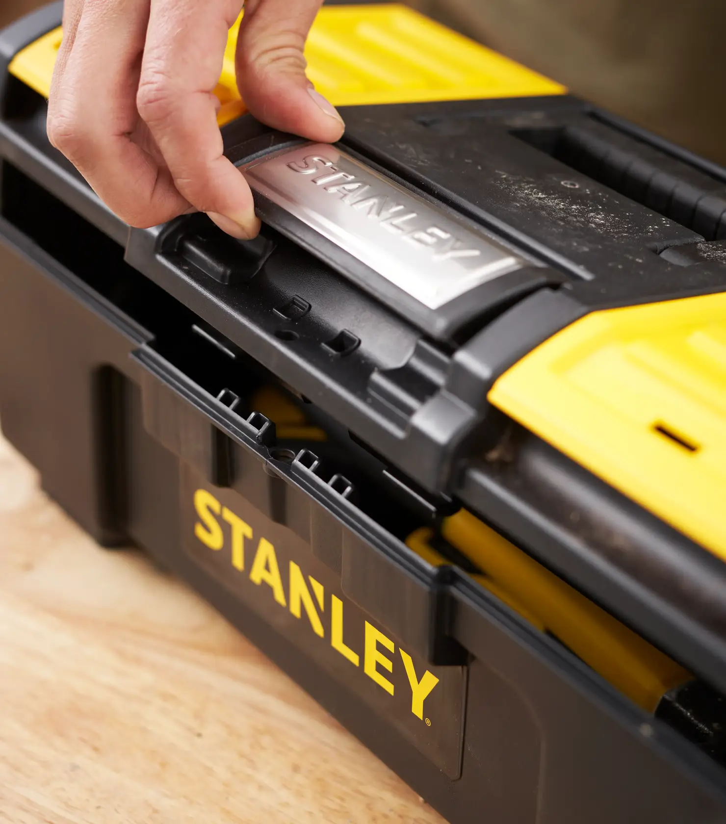 Photo de la boîte à outils STANLEY 1-79-216 noir et jaune, zoom sur le loquet ouvert sur la table.