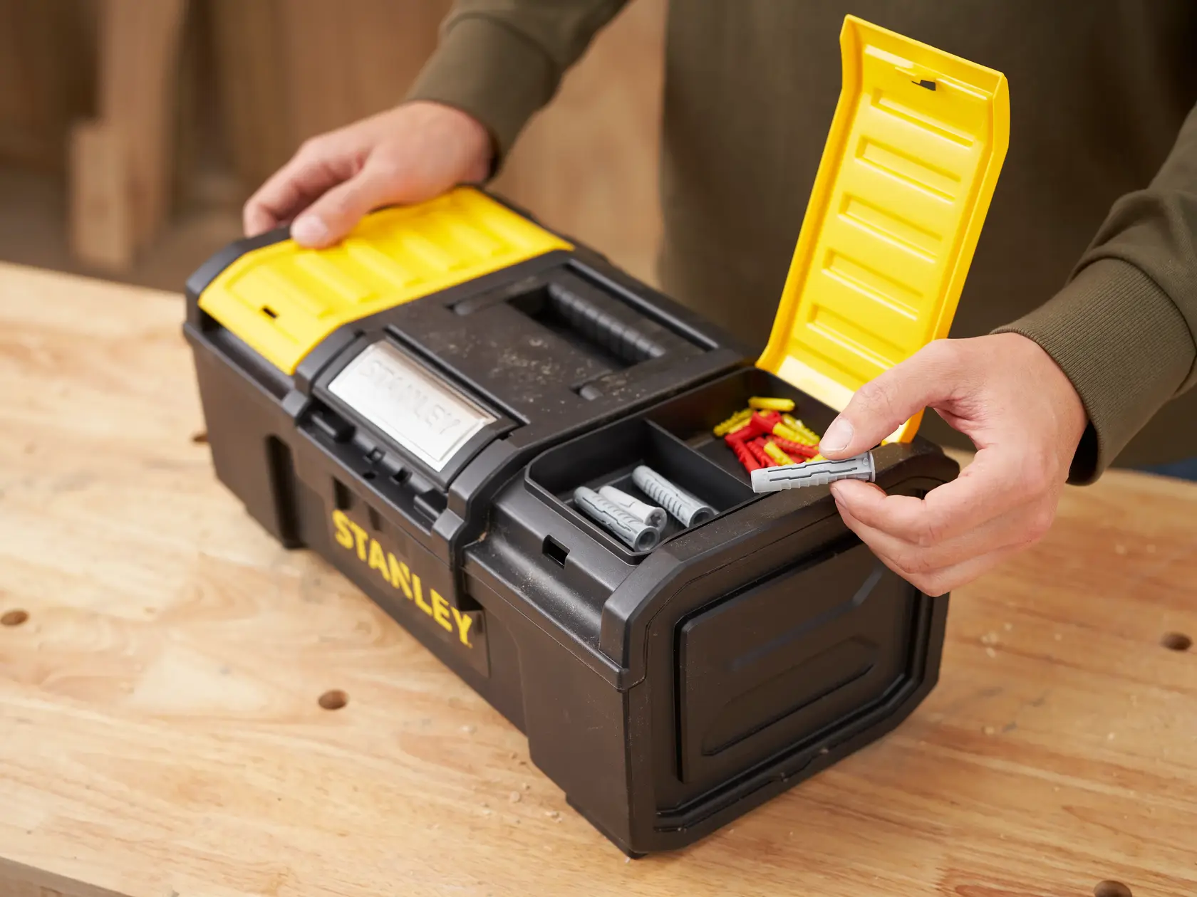 STANLEY 1-79-216 boîte à outils noire et jaune, couvercle ouvert, compartiments avec chevilles sur établi.