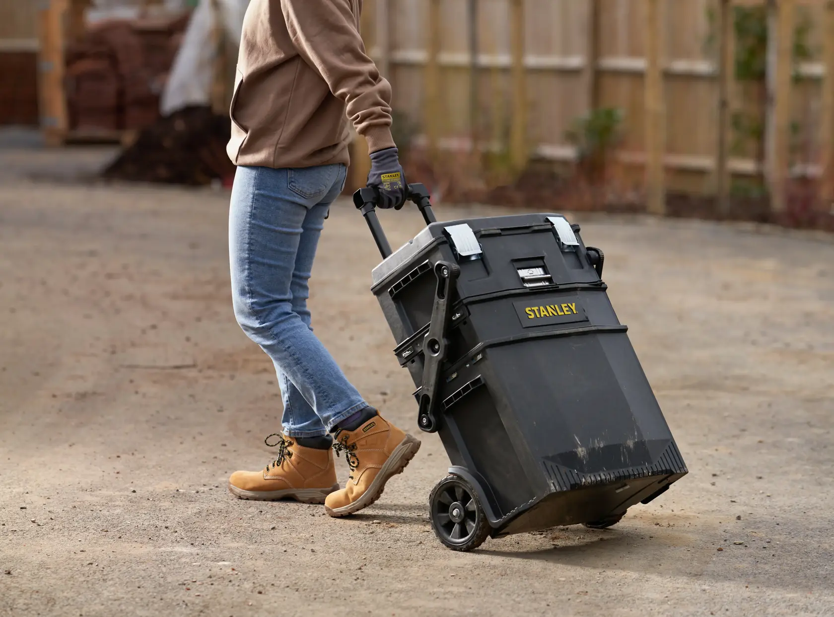 STANLEY 1-94-210 boîte à outils roulante tirée à l’extérieur par une personne en jean et bottes de travail.