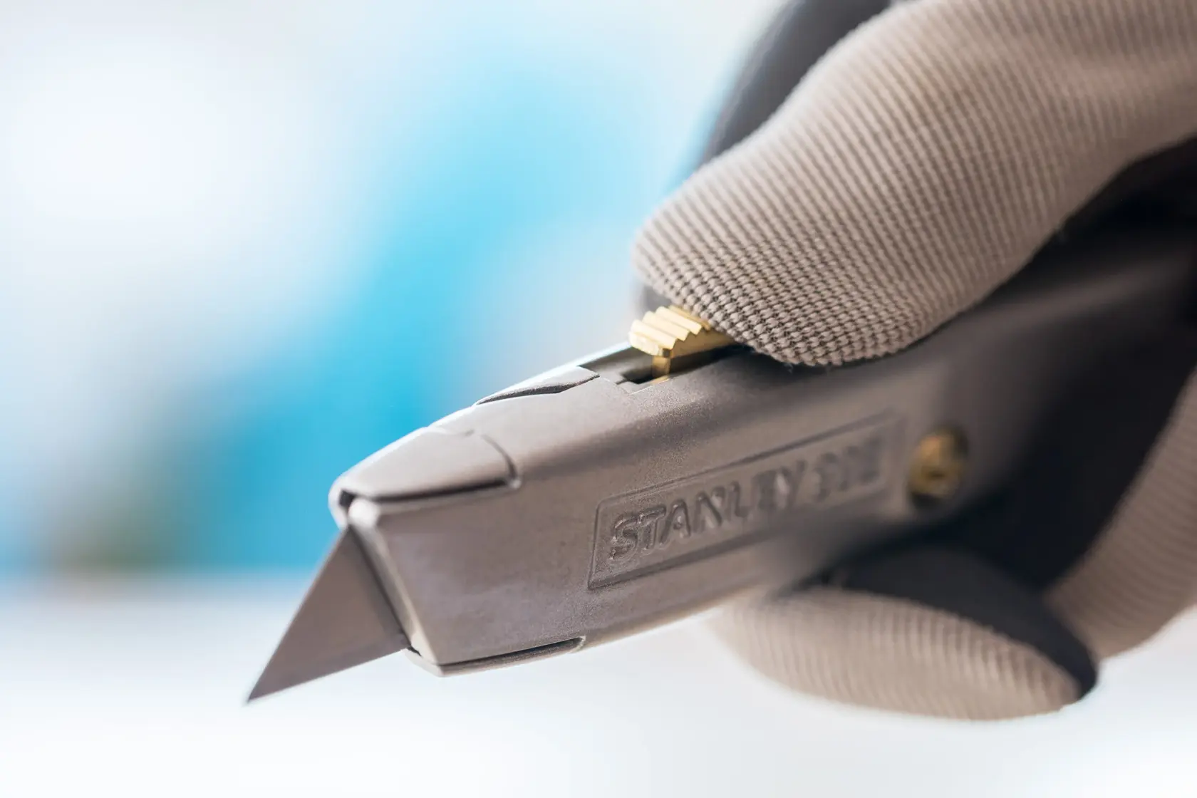 Nahaufnahme vom STANLEY 2-10-099 Universalmesser in behandschuhter Hand, mit Metallgehäuse und herausstehender Klinge.