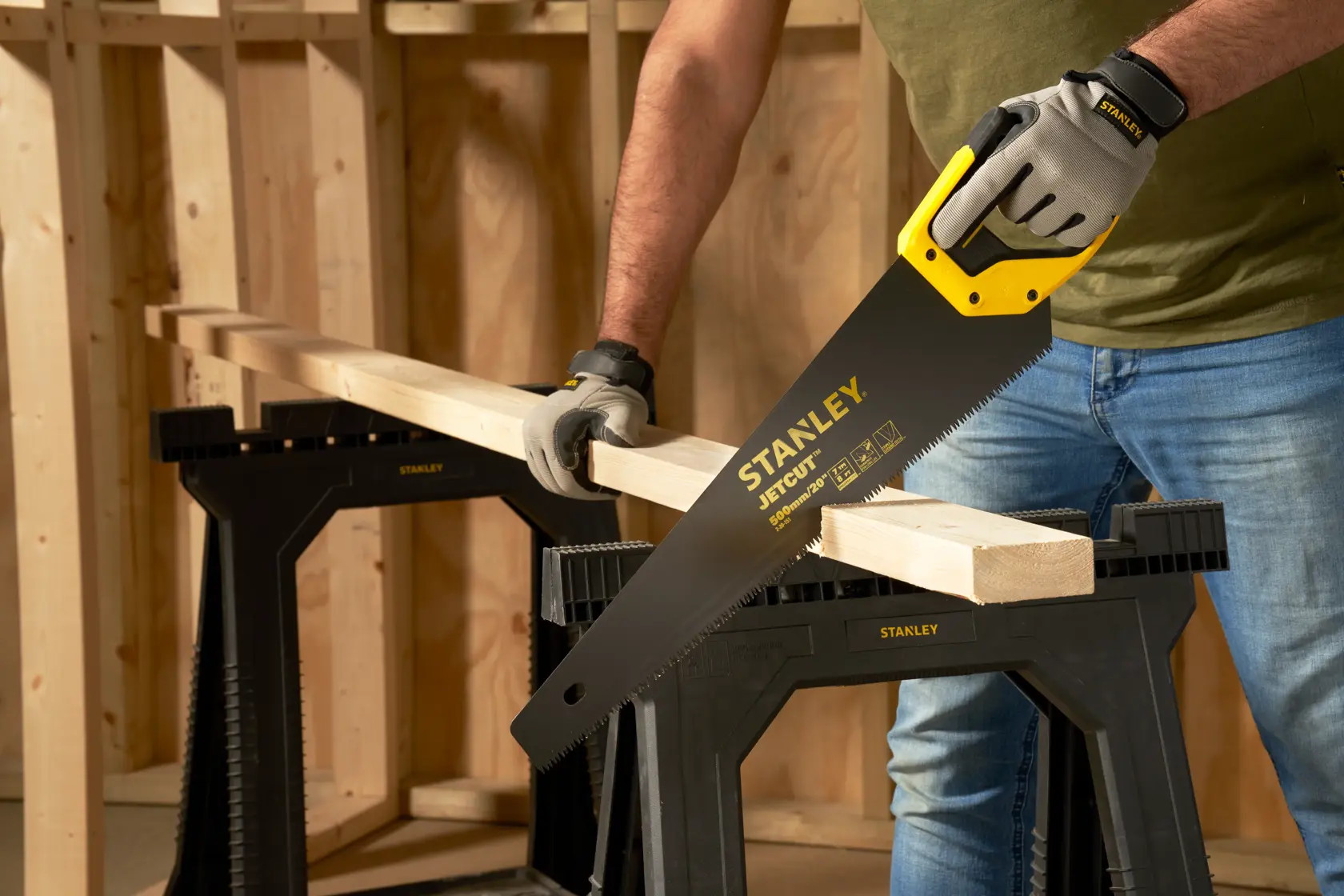 Photo de STANLEY 2-20-151 scie à main coupant une planche, gants, tréteaux en bois dans atelier.