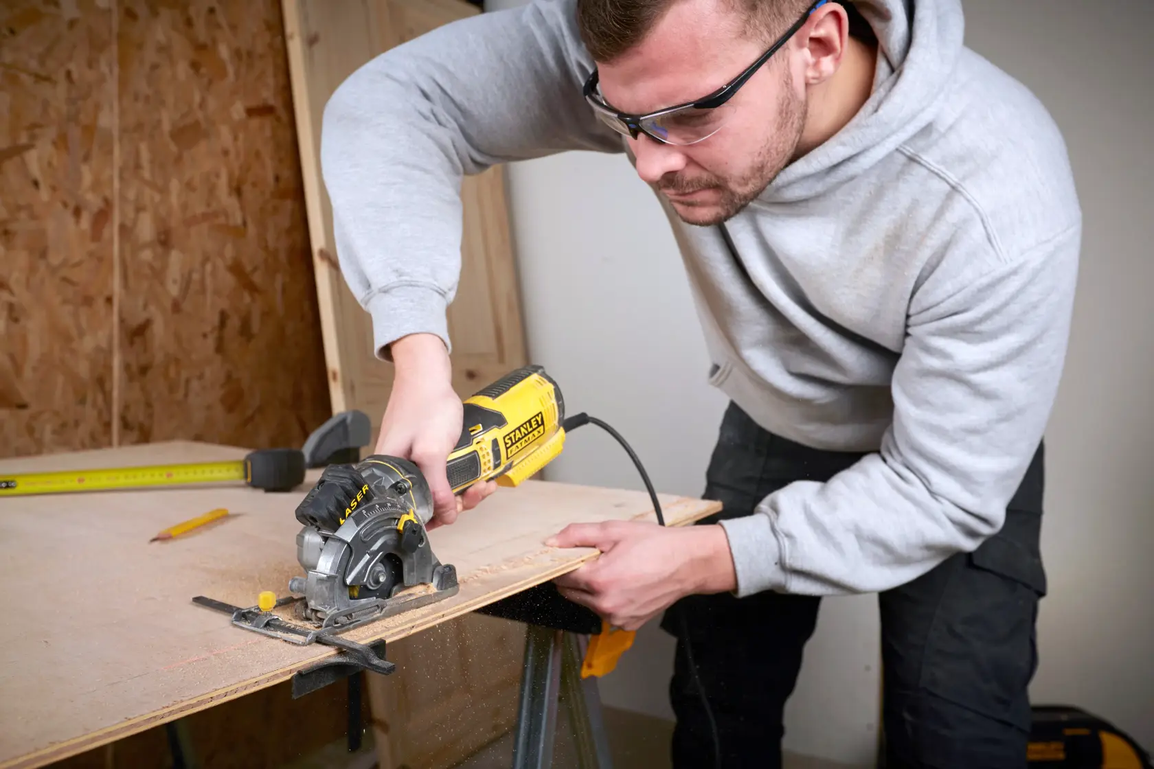 STANLEY FME380K circular saw in use cutting plywood, close-up of tool held by person in workshop.