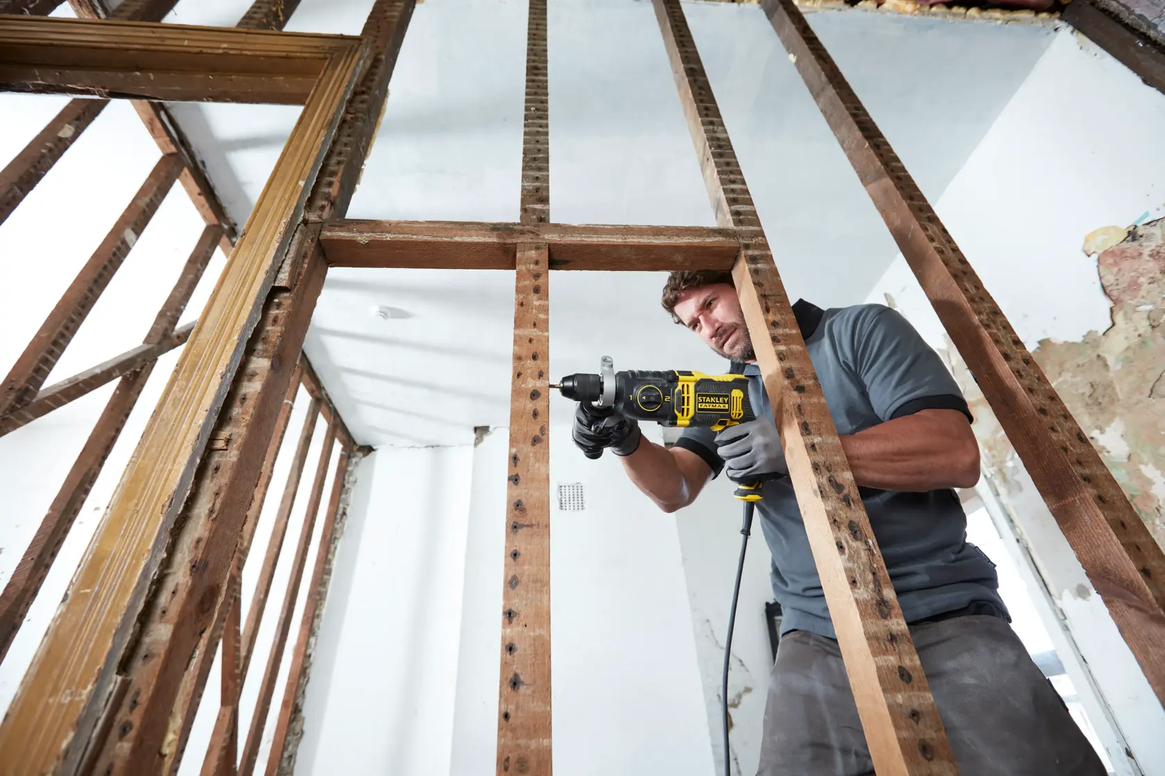 STANLEY FMEH750K corded hammer drill used in construction, shown through wooden wall studs.