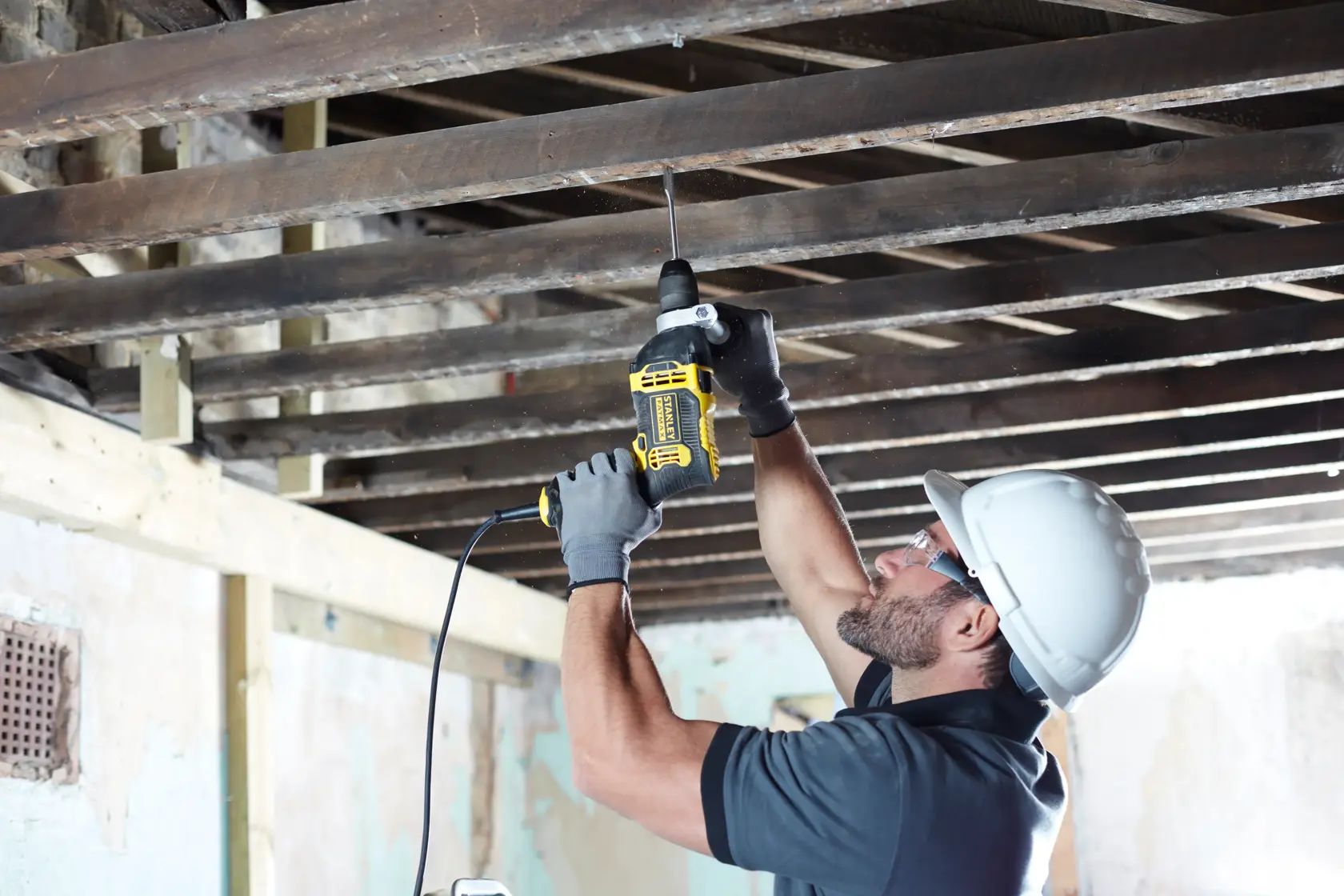 STANLEY FMEH750K corded drill used overhead on wooden beams, side angle, construction setting.