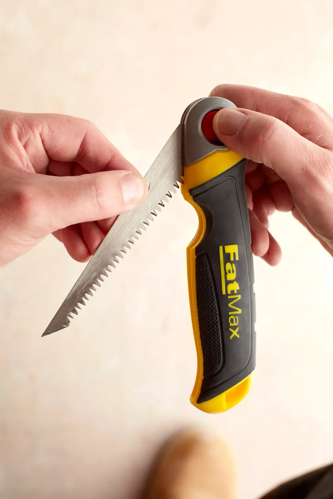 STANLEY FMHT0-20559 folding hand saw with black and yellow FatMax handle held in hand, angled close-up.