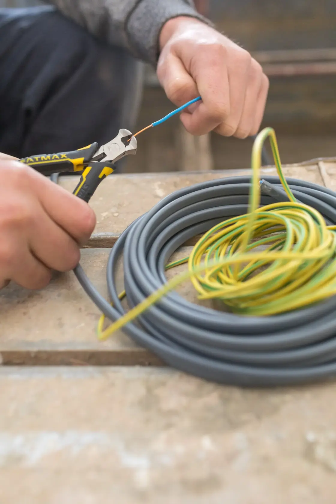 STANLEY FMHT0-80519 pliers cutting wire, close-up photo with coiled electrical cables on workbench.