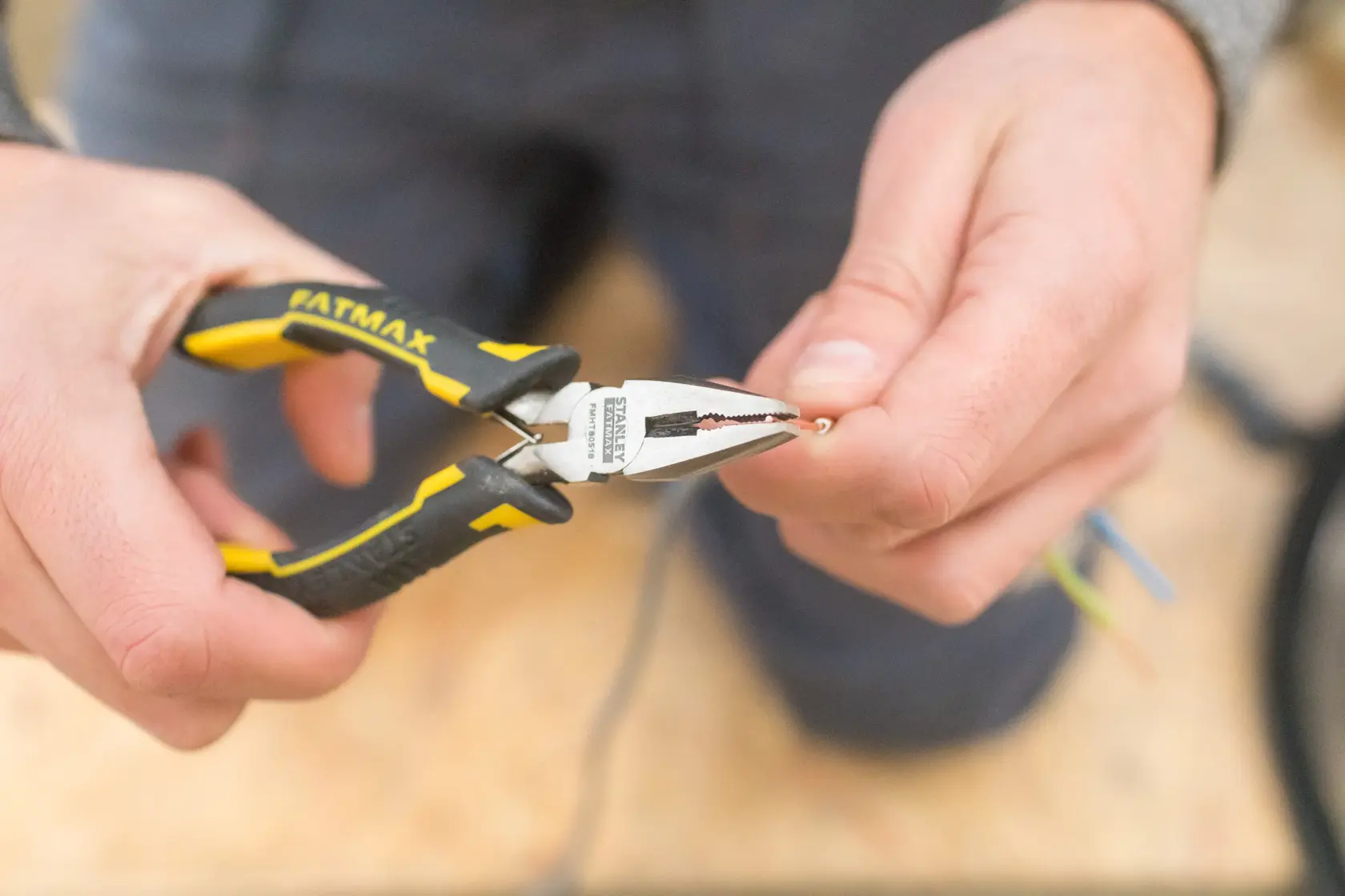 STANLEY FMHT0-80524 pliers with yellow and black handle gripping wire, close-up in hand.