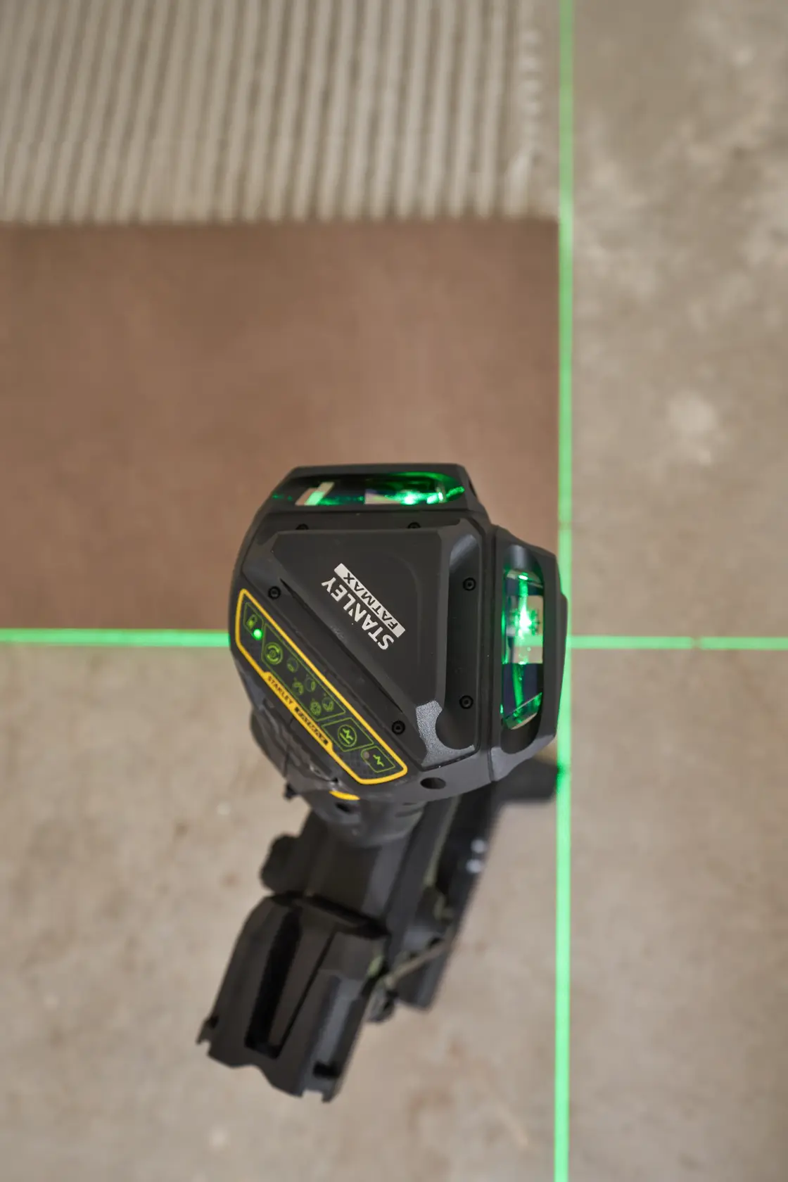 STANLEY FMHT1-77356 laser level projecting bright green lines onto a tiled floor, top view.