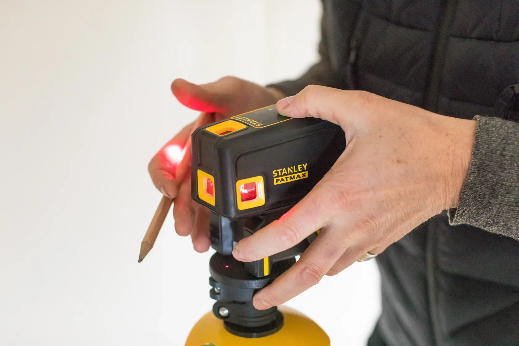 Photo of STANLEY FMHT1-77413 laser level in use, hand adjusting device, yellow and black housing.