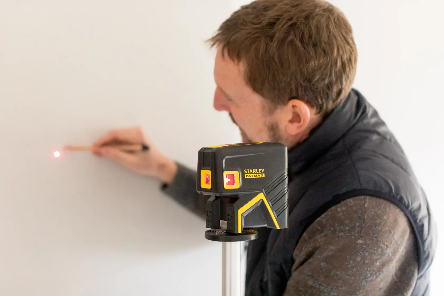 STANLEY FMHT1-77413 laser level on tripod projecting red dot, user marking spot on wall.