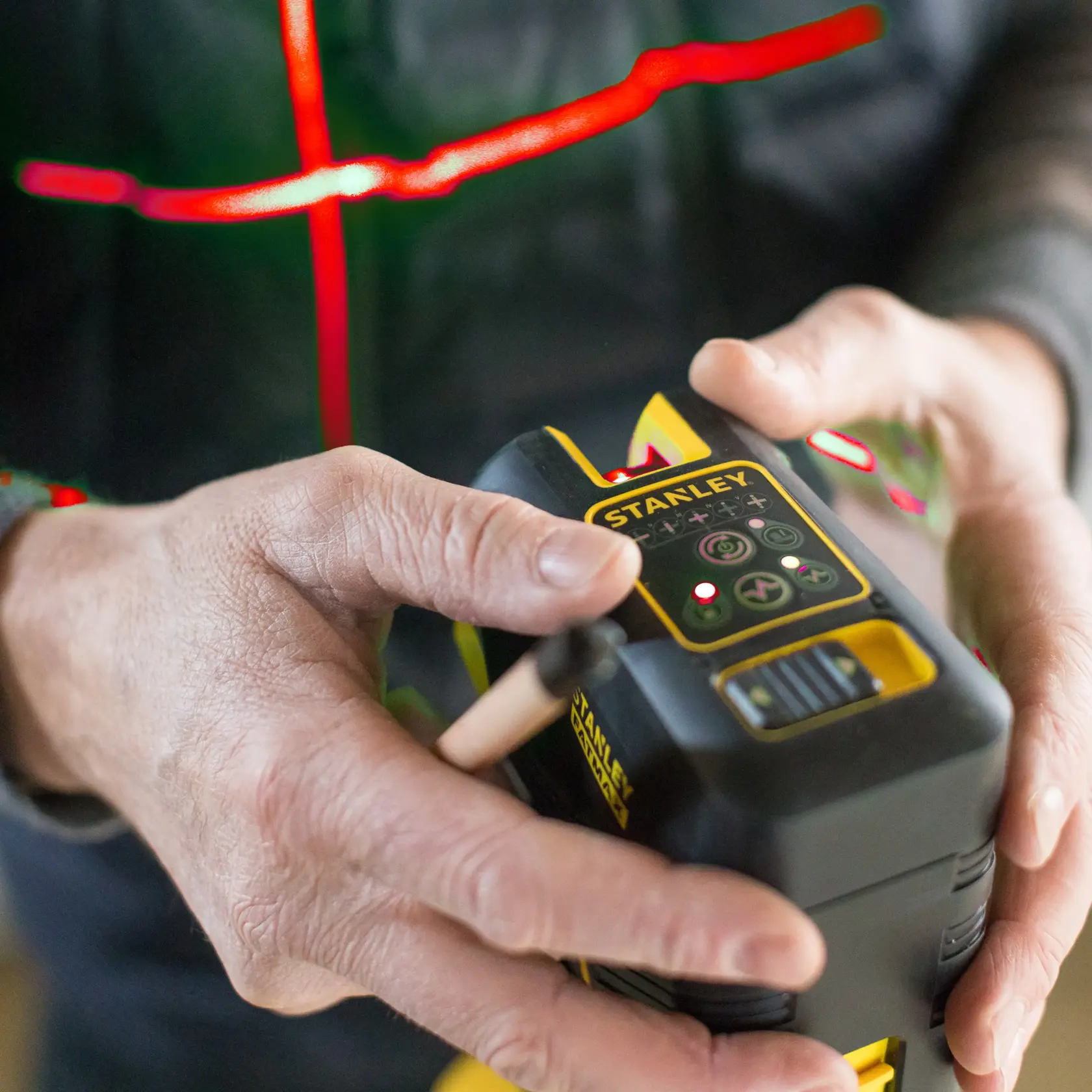 Photo of STANLEY FMHT1-77414 laser level held in hand, front control buttons and branding visible.