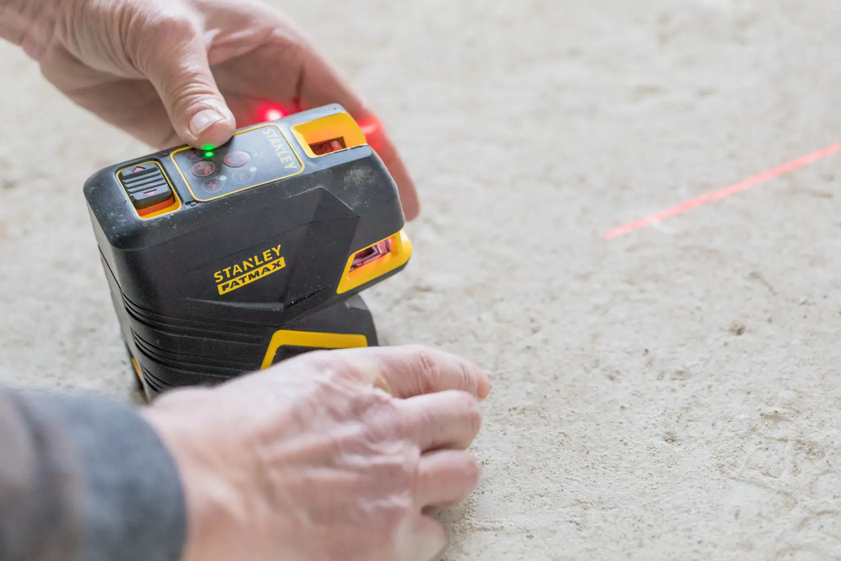 Photo of STANLEY FMHT1-77415 laser level on floor in use, projecting red laser line.