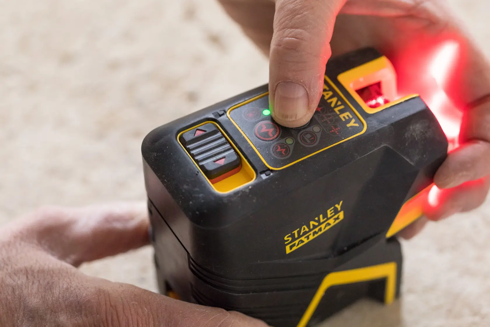 Photo of STANLEY FMHT1-77415 laser level being operated by hand on beige surface.