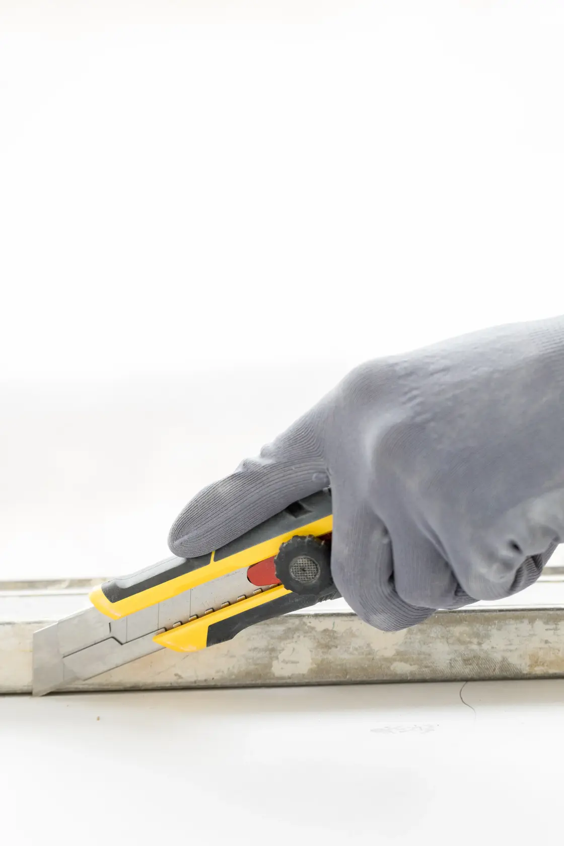 Photo of STANLEY FMHT10330-0 utility knife in gloved hand cutting along a metal guide.