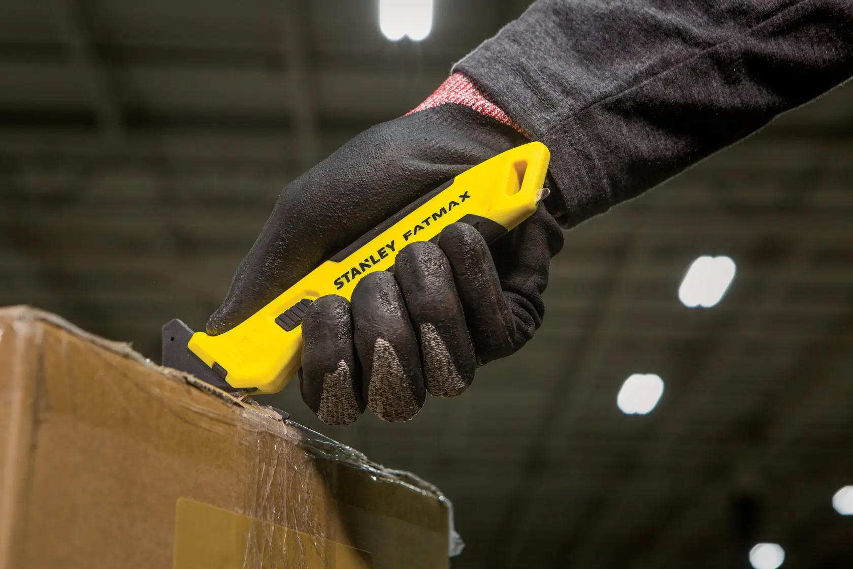STANLEY FMHT10358-0 utility knife with yellow handle cutting box, shown held in gloved hand.