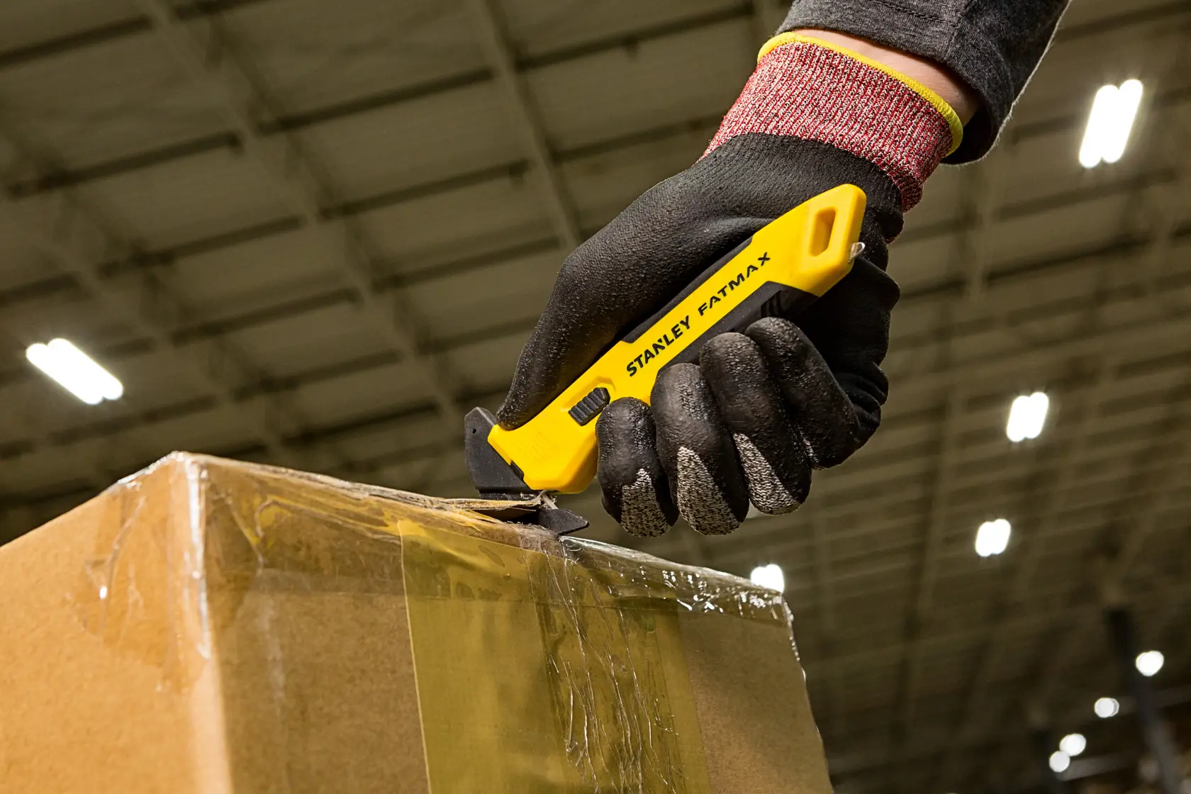 STANLEY FMHT10358-0 utility knife cutting tape on a cardboard box, worker wearing black gloves.