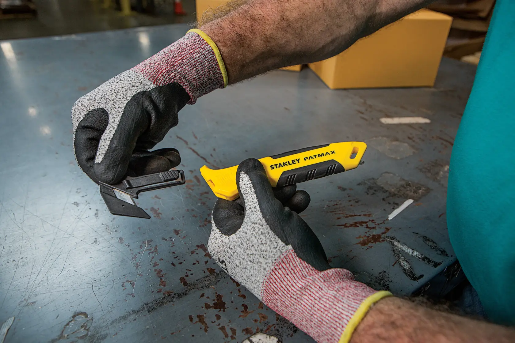 Photo of STANLEY FMHT10358-0 utility knife with yellow handle being held by gloved hands on a metal table.