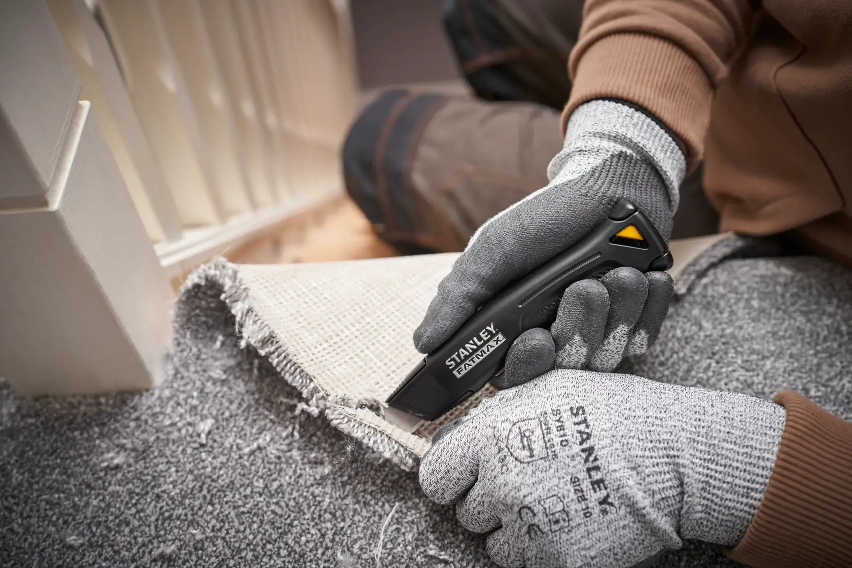 Foto des STANLEY FMHT10500-0 Universalmessers beim Schneiden von Teppich, behandschuhte Hände halten Messer und Teppich.
