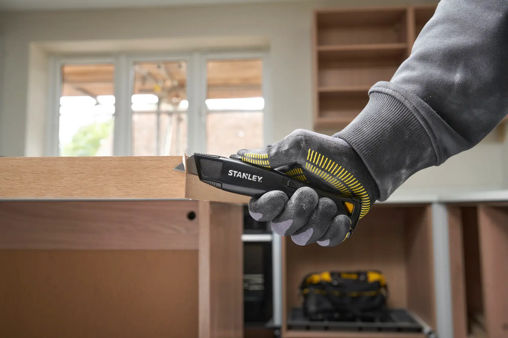 Couteau utilitaire STANLEY FMHT10504-0 dans une main gantée coupant du bois, intérieur, vue latérale du produit.