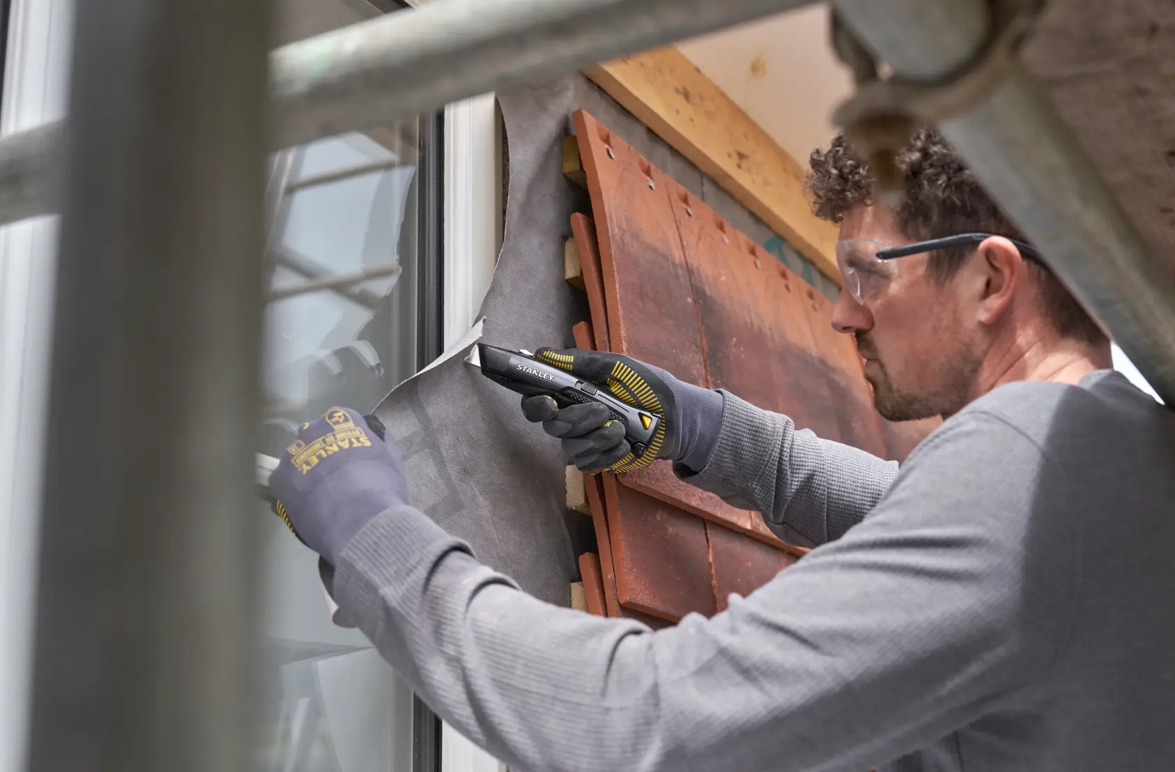 Cutter STANLEY FMHT10504-0 utilisé pour couper une membrane de bâtiment près d'une fenêtre, gros plan lors de travaux.